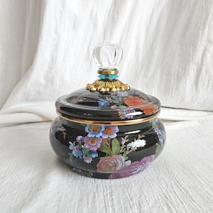 May include: A black ceramic jar with a lid, adorned with a floral pattern in shades of red, purple, blue, and white. The lid is topped with a clear, faceted knob and gold-colored accents. The jar has a gold rim.