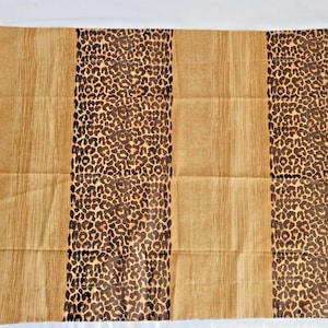 May include: A brown and tan fabric with a leopard print pattern. The fabric has three vertical stripes of the leopard print pattern, with the rest of the fabric being a solid brown and tan color.