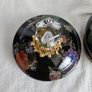 May include: A black ceramic lid with a floral design featuring red, blue, and purple flowers. The lid has a clear, faceted knob with a gold-colored base. The design is reminiscent of vintage porcelain.