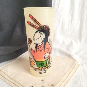 May include: Vintage frosted glass tumbler featuring a cartoon Native American figure. The illustration includes a figure in a pink shirt, green skirt, and a feathered headdress. The word "DOCTOR" is printed at the bottom of the glass.