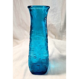 May include: A tall, turquoise blue glass vase with a geometric pattern. The vase has a narrow neck and a wide base.