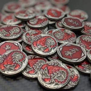 May include: A pile of silver-coloured tokens with red scorpion designs and Chinese characters. The tokens have a raised edge and a smooth surface.