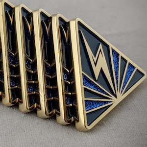 May include: A set of ten gold-colored pins with a black and blue enamel design. The pins feature a stylized lightning bolt and a geometric pattern.