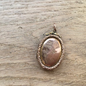 May include: A gold oval locket with an ornate design and a profile of a person engraved on the front.