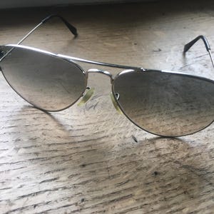 K&ouml;nnte beinhalten: Silberne Aviator-Sonnenbrille mit grauen Verlaufsgl&auml;sern.
