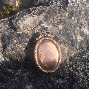 May include: An oval-shaped gold locket with an ornate design and a floral pattern engraved on the front.