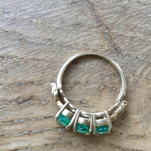 Pu&ograve; includere: Un anello d'oro con tre pietre preziose verde smeraldo incastonate a griffe.