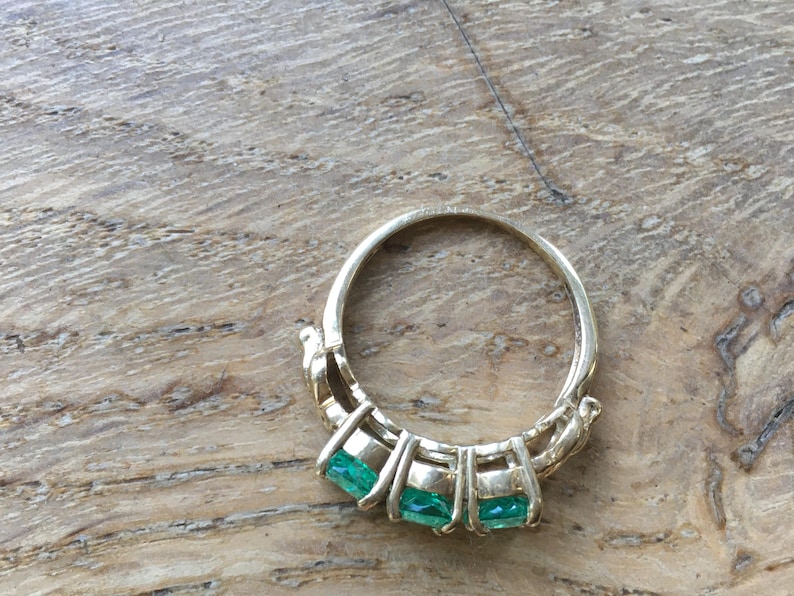 Pu&ograve; includere: Un anello d'oro con tre pietre preziose verde smeraldo incastonate a griffe.
