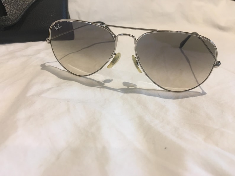 K&ouml;nnte beinhalten: Silberne Aviator-Sonnenbrille mit braunen Verlaufsgl&auml;sern. Die Sonnenbrille liegt auf einer wei&szlig;en Oberfl&auml;che.