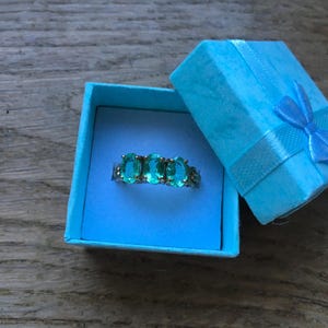 Pu&ograve; includere: Un anello turchese con pietre ovali incastonate in argento. L'anello &egrave; in una scatola per anelli blu chiaro con un nastro blu chiaro.
