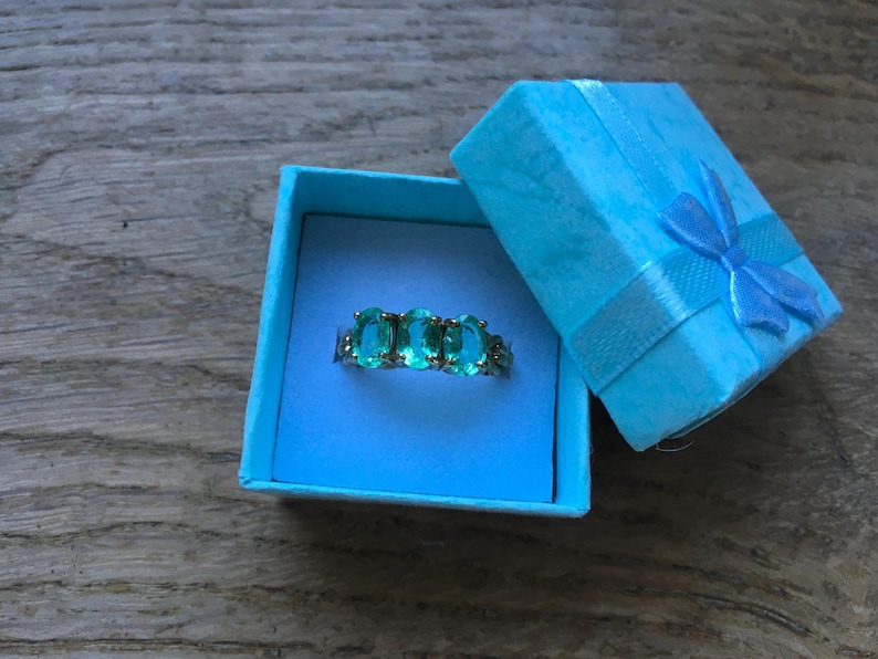 Pu&ograve; includere: Un anello turchese con pietre ovali incastonate in argento. L'anello &egrave; in una scatola per anelli blu chiaro con un nastro blu chiaro.