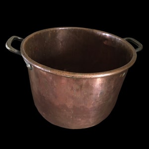 May include: A large copper pot with two metal handles. The pot has a worn, aged appearance.