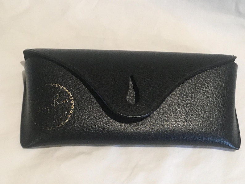 K&ouml;nnte beinhalten: Schwarzes Lederetui mit einem goldgepr&auml;gten Logo. Das Etui hat eine Klappe mit einem Ausschnitt.