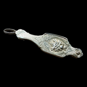 Op de afbeelding: Een sierlijke, decoratieve sluiting van zilver met een bloemmotief. De sluiting heeft aan de ene kant een lus en aan de andere kant een haak.