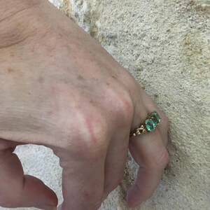 Pu&ograve; includere: Un anello d'oro con tre pietre preziose verdi incastonate in un design delicato.