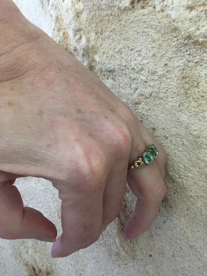 Pu&ograve; includere: Un anello d'oro con tre pietre preziose verdi incastonate in un design delicato.
