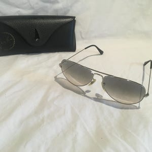 K&ouml;nnte beinhalten: Silberne Aviator-Sonnenbrille mit grauen Verlaufsgl&auml;sern und einem schwarzen Lederetui.