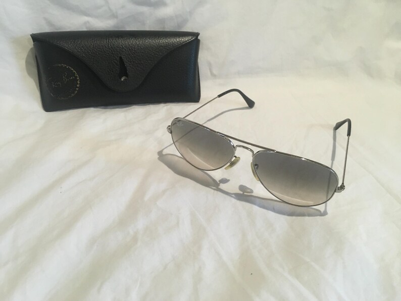 K&ouml;nnte beinhalten: Silberne Aviator-Sonnenbrille mit grauen Verlaufsgl&auml;sern und einem schwarzen Lederetui.