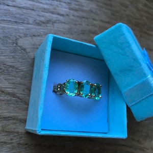 Pu&ograve; includere: Un anello con tre pietre ovali color turchese incastonate in argento. L'anello &egrave; in una scatola per anelli in velluto blu chiaro.