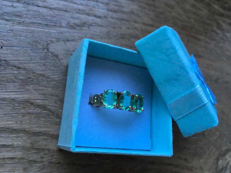 Pu&ograve; includere: Un anello con tre pietre ovali color turchese incastonate in argento. L'anello &egrave; in una scatola per anelli in velluto blu chiaro.