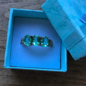 Pu&ograve; includere: Un anello turchese con cinque pietre ovali incastonate in una fascia d'argento. L'anello &egrave; esposto in una scatola per anelli blu chiaro con un nastro blu.
