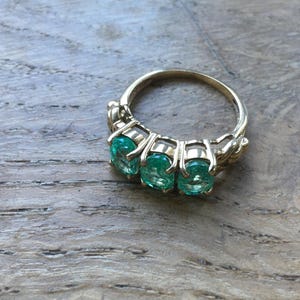Pu&ograve; includere: Un anello d'oro con tre pietre preziose verde smeraldo incastonate a griffe.