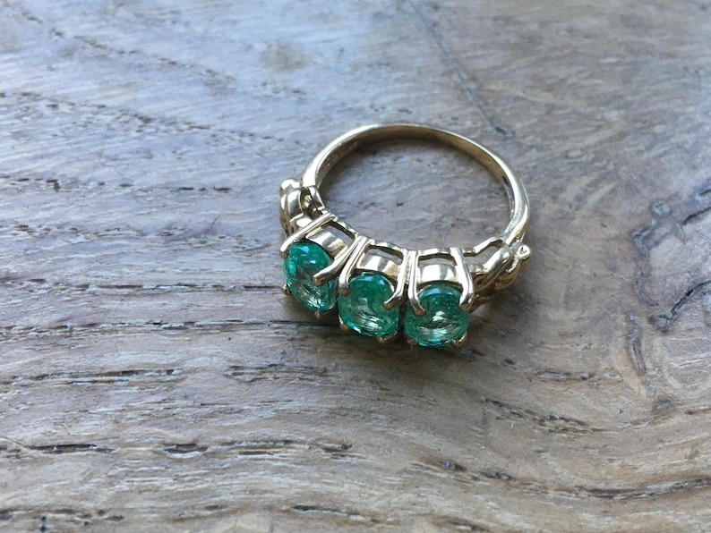 Pu&ograve; includere: Un anello d'oro con tre pietre preziose verde smeraldo incastonate a griffe.