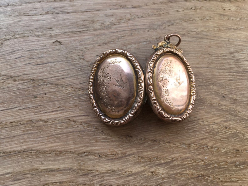 May include: A gold oval locket with an engraved floral design and a bird on the front. The back of the locket has an inscription that reads "S.L.T. 1877".