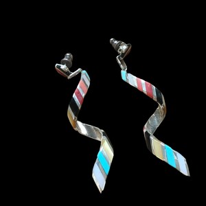 May include: A pair of silver dangle earrings with a twisted design. The earrings are decorated with inlaid turquoise, coral, and black stones.