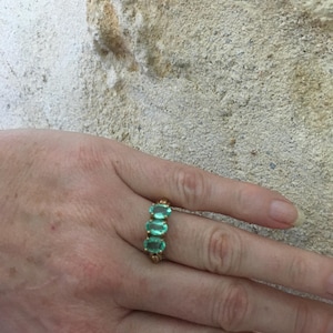 Pu&ograve; includere: Un anello d'oro con quattro pietre preziose verdi di forma ovale. L'anello &egrave; su un dito.