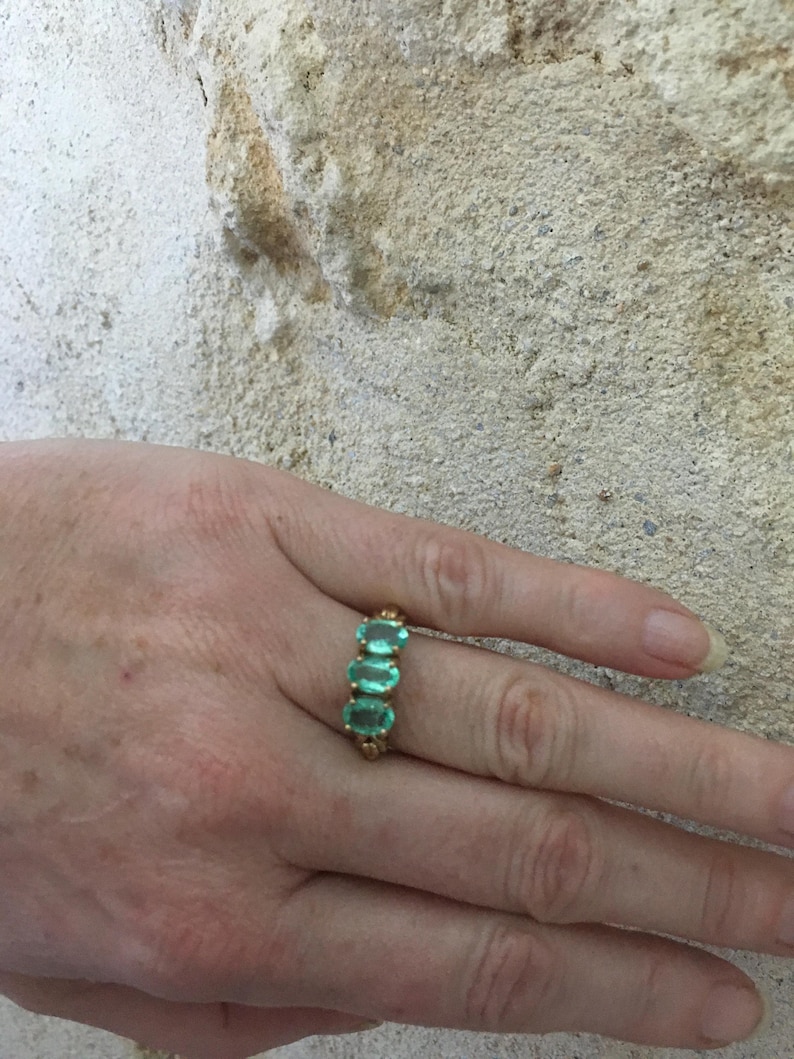 Pu&ograve; includere: Un anello d'oro con quattro pietre preziose verdi di forma ovale. L'anello &egrave; su un dito.