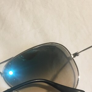 K&ouml;nnte beinhalten: Silberne Aviator-Sonnenbrille mit grauen Verlaufsgl&auml;sern. Die Sonnenbrille hat einen silbernen Metallrahmen und schwarze B&uuml;gel.
