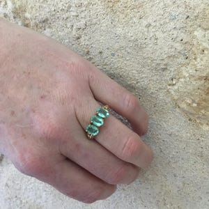 Pu&ograve; includere: Un anello d'oro con cinque pietre ovali di colore verde chiaro disposte in fila.