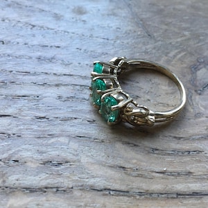 Pu&ograve; includere: Un anello d'oro con cinque pietre preziose verde smeraldo incastonate in un design delicato e ornato.
