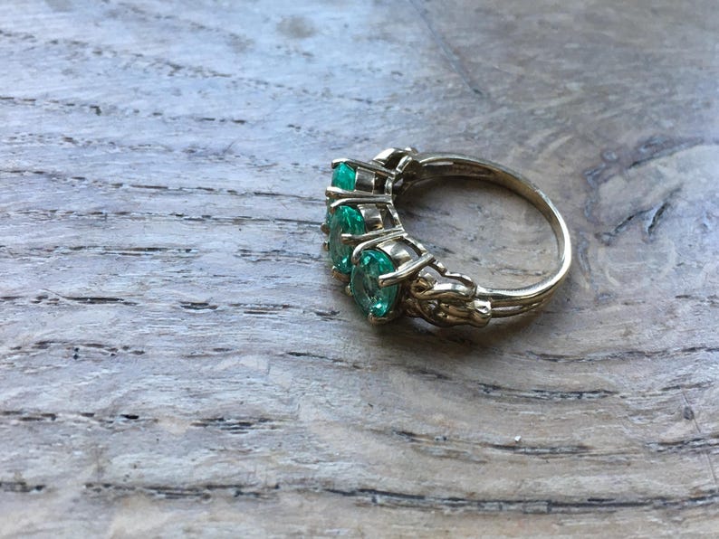Pu&ograve; includere: Un anello d'oro con cinque pietre preziose verde smeraldo incastonate in un design delicato e ornato.