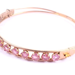 Puede incluir: Un brazalete de oro con una fila de piedras preciosas rosas.