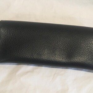 K&ouml;nnte beinhalten: Eine schwarze Leder-Clutch mit strukturierter Oberfl&auml;che.
