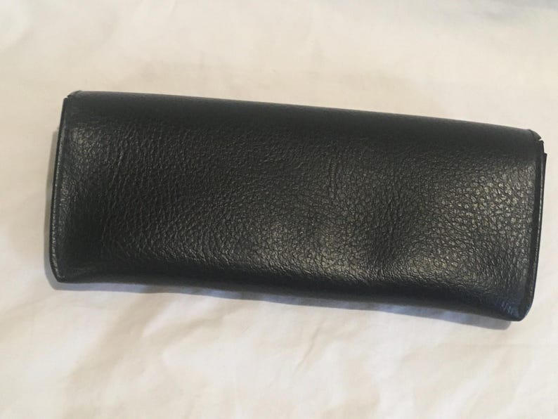 K&ouml;nnte beinhalten: Eine schwarze Leder-Clutch mit strukturierter Oberfl&auml;che.