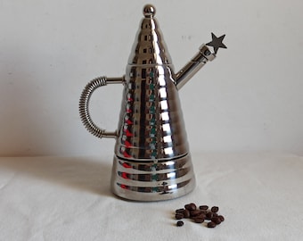 May include: A silver, cone-shaped coffee maker with a star-shaped handle and a spring-loaded handle. Coffee beans are scattered on a white surface.