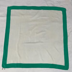May include: A square, off-white scarf with a vibrant green border. The scarf is made of a soft, possibly silk-like material, and is laid flat. The green border frames the off-white center, creating a simple yet elegant design.