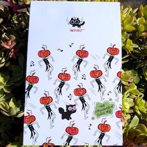 Può includere: Una carta bianca con un'illustrazione a fumetti di figure danzanti con teste di zucca in abiti neri. È presente anche un gatto nero con grandi occhi. Il testo "The Halloween Flash Mob" è in un fumetto. È presente anche il nome dell'artista, "Scarecat".