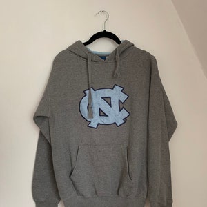 May include: Gray hooded sweatshirt with a blue and white North Carolina Tar Heels logo on the front.
