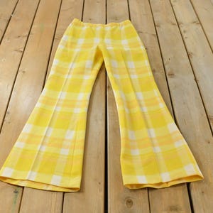 May include: A pair of bright yellow and white plaid trousers featuring a high-waisted design with a flared leg silhouette. The pants display a consistent checkered pattern throughout, with a clean waistband and straight seams running down the front.