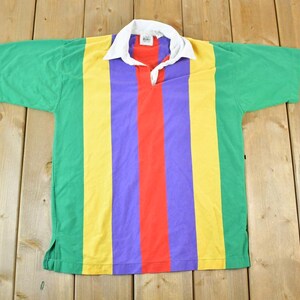 May include: A short-sleeved shirt with a white collar and a vibrant colour scheme. The shirt has vertical stripes in green, yellow, purple, and red. The garment is made of a soft material, suitable for casual wear.