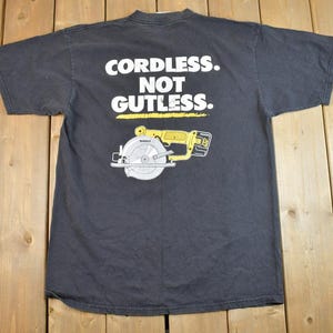 May include: Black t-shirt with a white graphic of a cordless circular saw and the text "Cordless. Not Gutless."