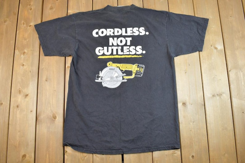 May include: Black t-shirt with a white graphic of a cordless circular saw and the text "Cordless. Not Gutless."