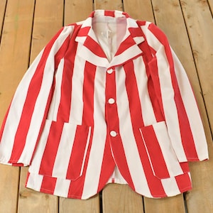 May include: A red and white striped blazer with three white buttons and two front pockets. The jacket is made of a lightweight fabric and has a classic, vintage style. The blazer is laid flat on a wooden surface.