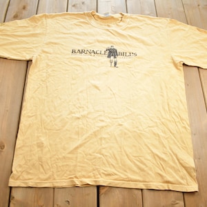 Może przedstawiać: Żółta koszulka z nadrukiem "Barnacle Bill's" na przodzie. Tekst jest czarny i otoczony czarną ramką.