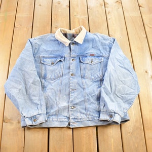Könnte beinhalten: Eine hellblaue Jeansjacke mit einem Cordkragen. Die Jacke hat einen Knopfverschluss und zwei Fronttaschen.