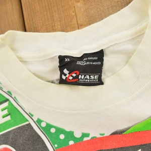 May include: White t-shirt with a green, red and black graphic print featuring the text "STATE" and a chequered flag. The shirt has a black tag with the text "CHASE AUTHENTICS" and the size "XL".